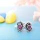 A pair of silver toe rings with purple cutstones set in a floral design.