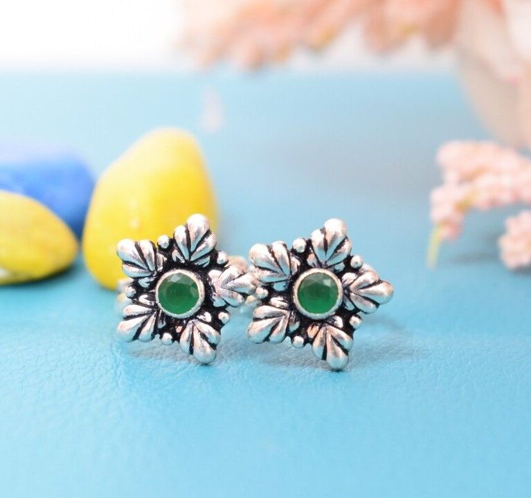 A pair of silver toe rings with green cutstones set in a star-shaped design.