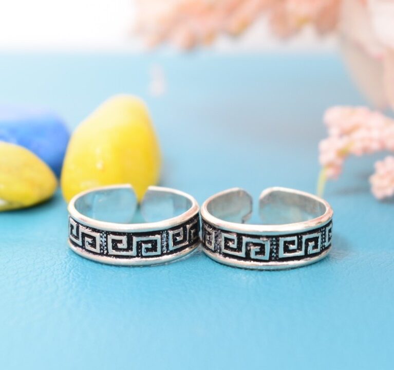 A pair of silver toe rings with a Greek key pattern engraved on the bands.