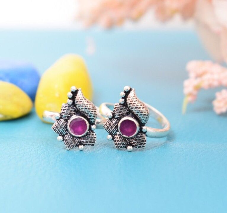 A pair of silver toe rings with purple cutstones set in a teardrop shape.