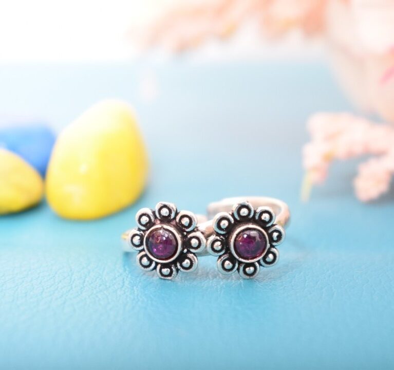 A pair of silver toe rings with purple stones set in a floral design.