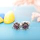 A pair of silver toe rings with purple stones set in a floral design.