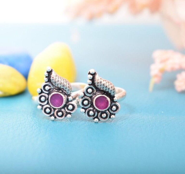 A pair of silver toe rings with purple stones set in a teardrop design.