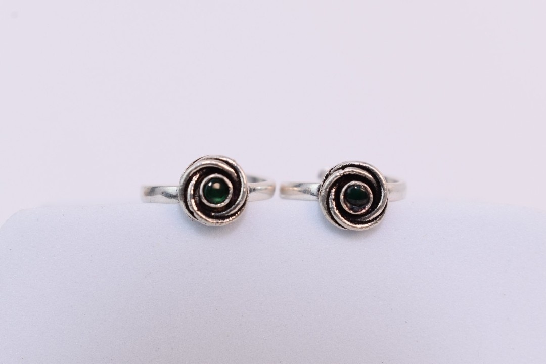 A pair of silver toe rings with green stones set in a spiral design