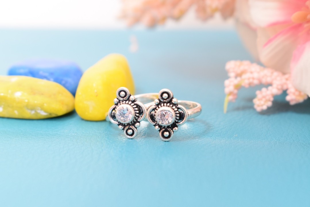 A pair of silver toe rings with white stones set in a geometric design.