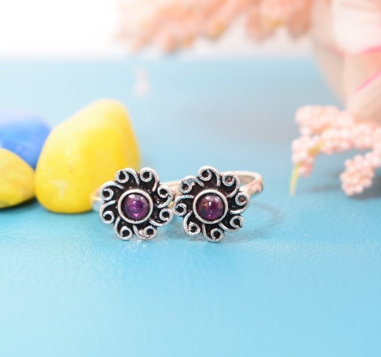 A pair of silver toe rings with purple stones set in a floral design.