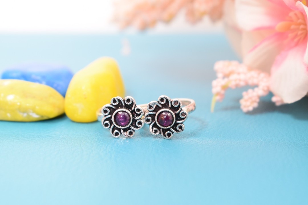 A pair of silver toe rings with purple stones set in a floral design.