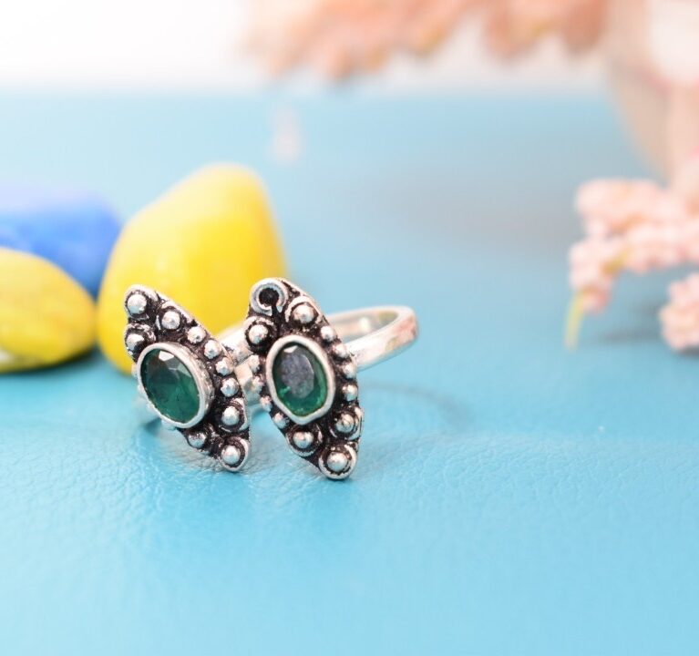 A pair of silver toe rings with green stones set in a marquise shape.