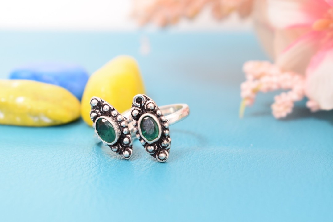A pair of silver toe rings with green stones set in a marquise shape.