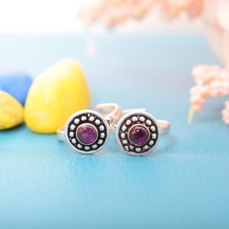 A pair of silver toe rings with purple stones set in a circular design.