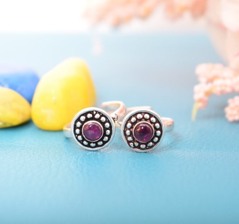 A pair of silver toe rings with purple stones set in a circular design.