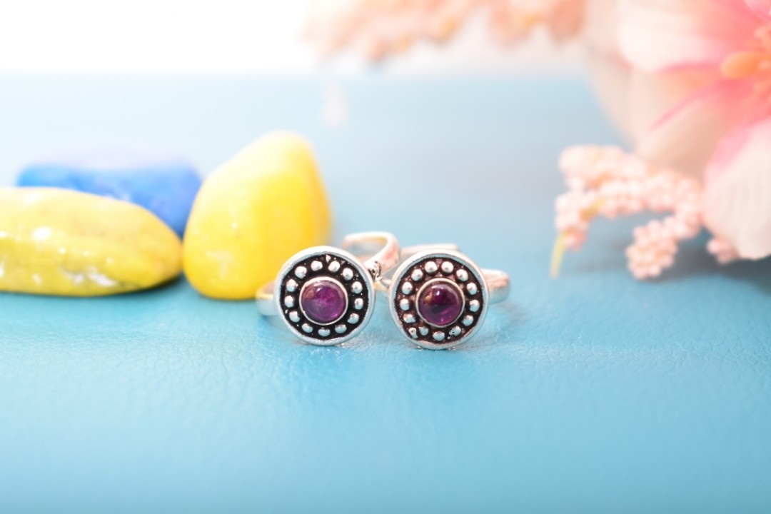 A pair of silver toe rings with purple stones set in a circular design.