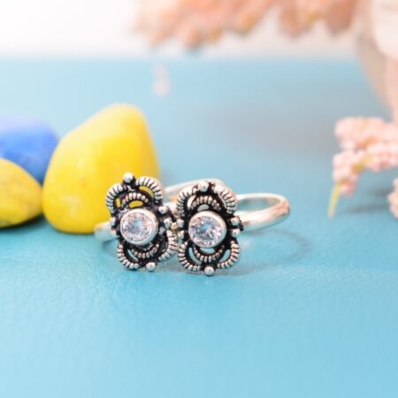 A pair of silver toe rings with white stones set in a floral design.