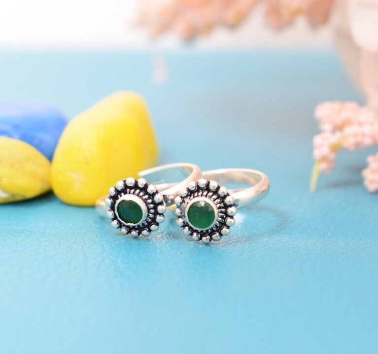 A pair of silver toe rings with green stones set in a circular design.