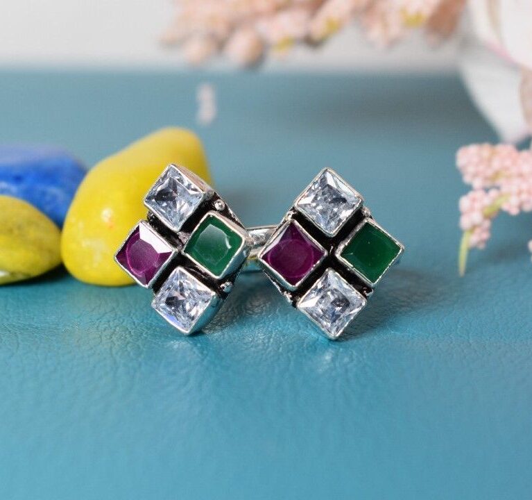 A pair of silver toe rings with a square design featuring white, green, and red cutstones.