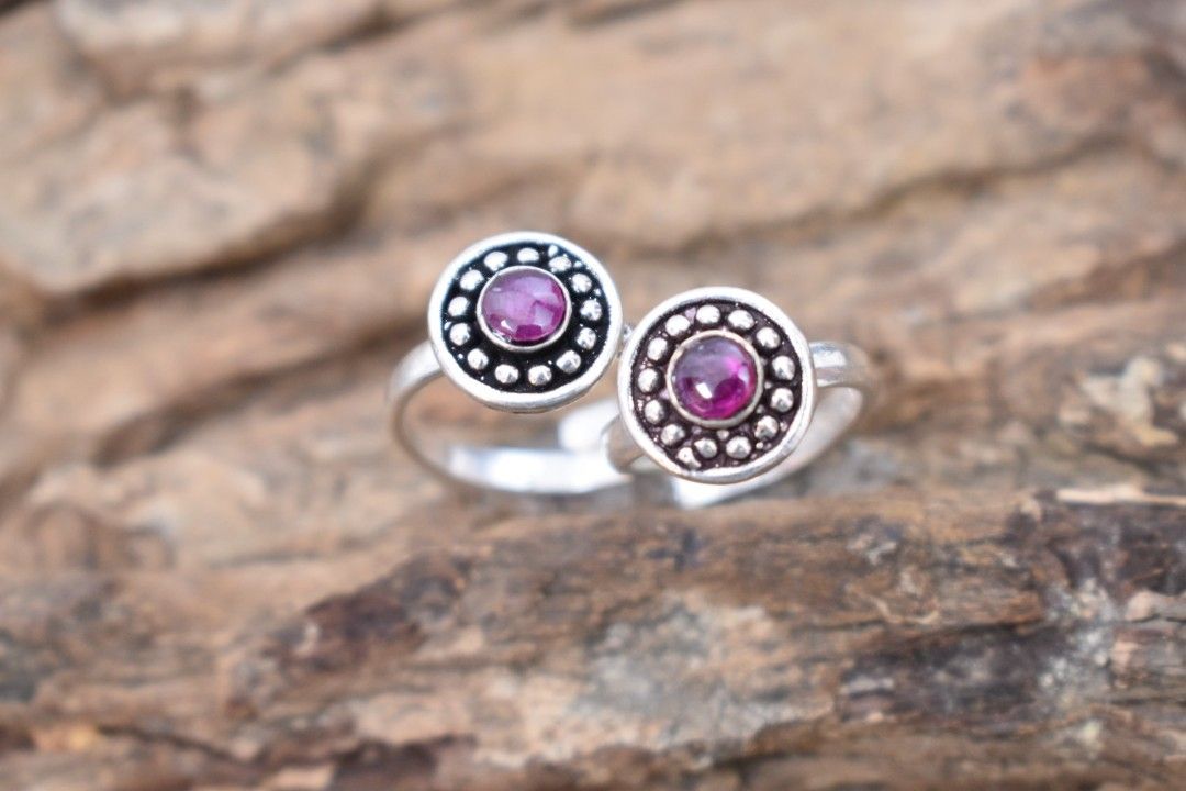 A pair of silver toe rings with purple stones set in a circular design.