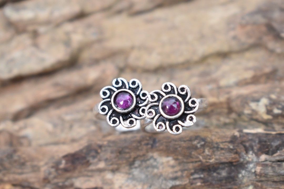 A pair of silver toe rings with purple stones set in a floral design.