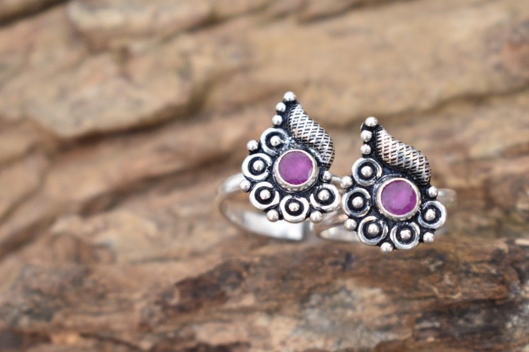 A pair of silver toe rings with purple stones set in a teardrop design.