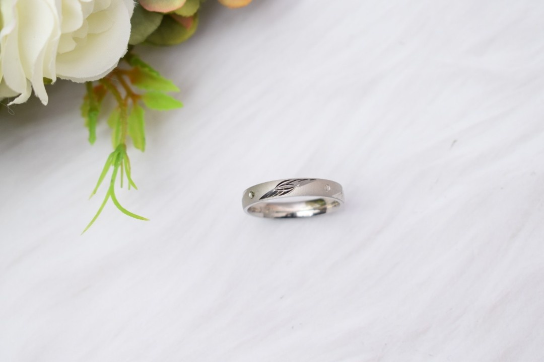 A silver ring with a delicate leaf design engraved on the band.