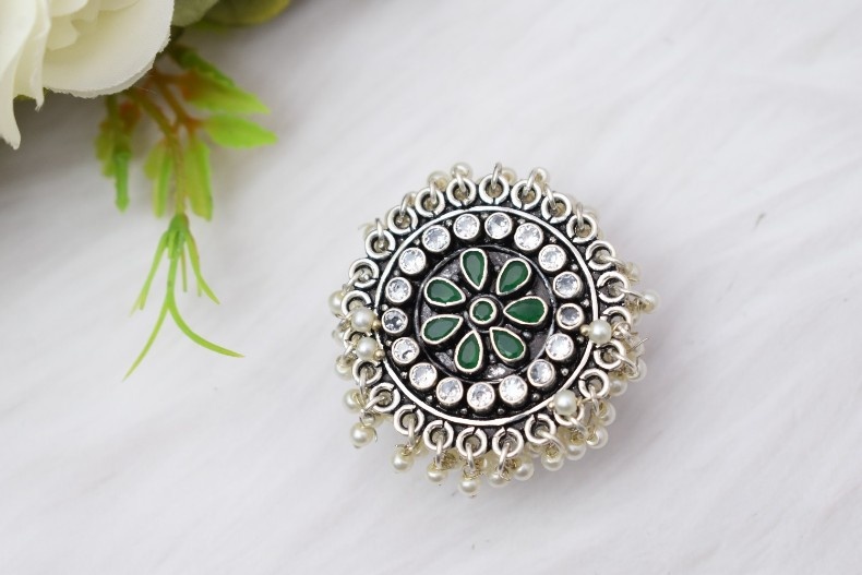 A silver ring with a circular design featuring green and white cutstones, adorned with pearls.