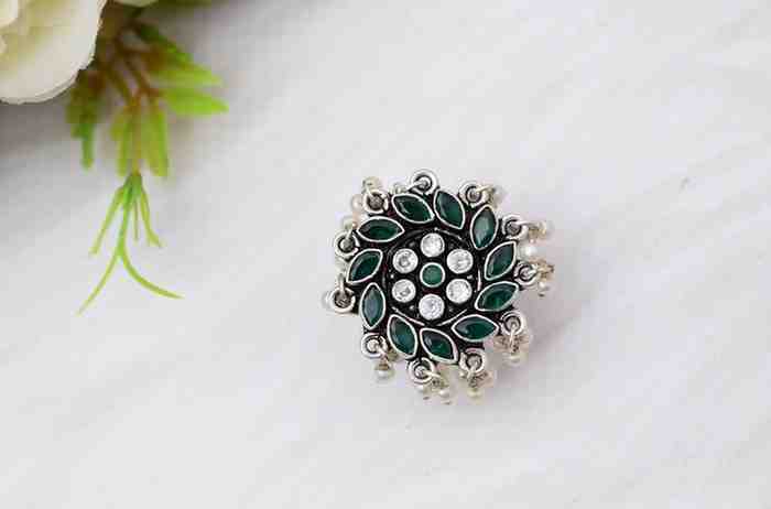 A silver ring with a circular design featuring green and white cutstones, adorned with pearls.