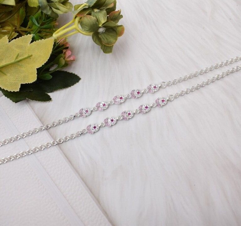 A pair of silver anklets with pink and white cutstones set in a circular design.