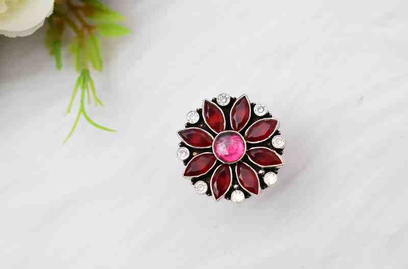 A silver ring with a floral design featuring red and pink cutstones surrounded by white cutstones.