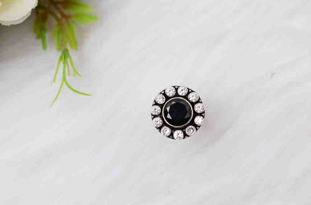 A silver ring with a circular design featuring a black cutstone surrounded by white cutstones.