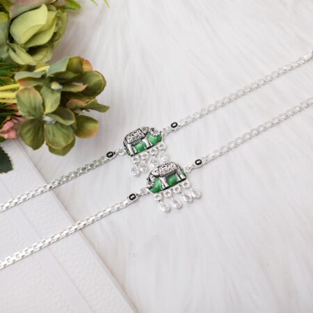 A pair of silver anklets with elephant-shaped pendants adorned with green enamel and white cutstones.