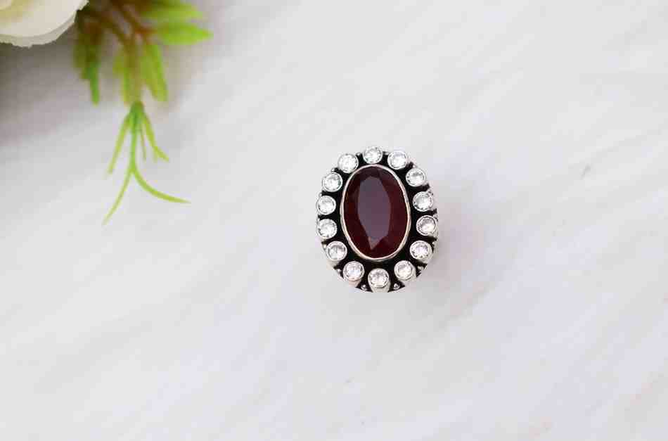 A silver ring with a large, oval-shaped red cutstone surrounded by smaller white cutstones.