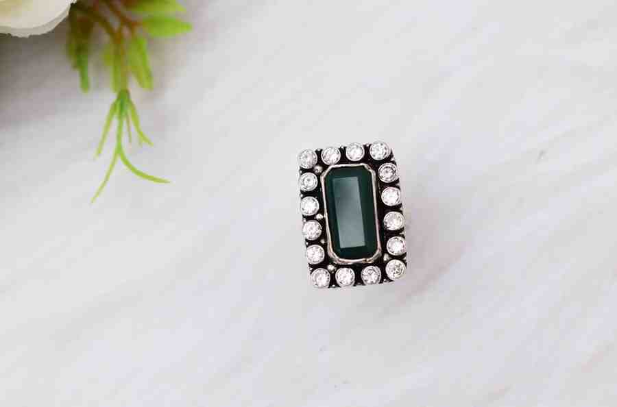 A silver ring with a rectangular green cutstone surrounded by white cutstones.