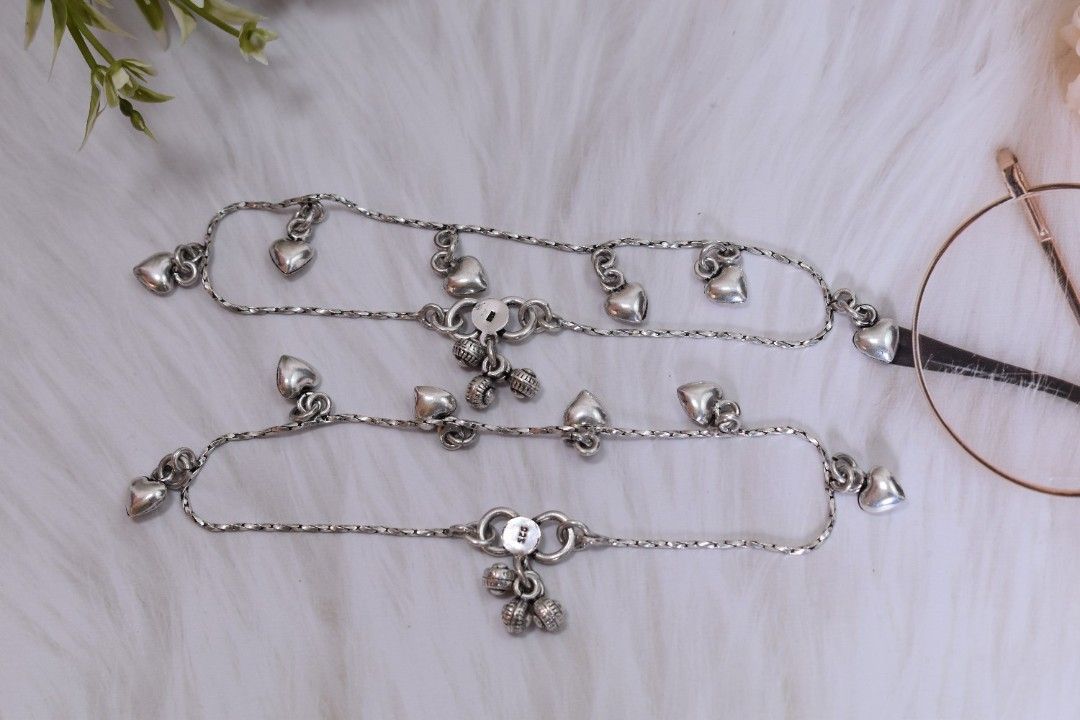 A pair of silver anklets with multiple heart-shaped pendants dangling from a delicate chain.