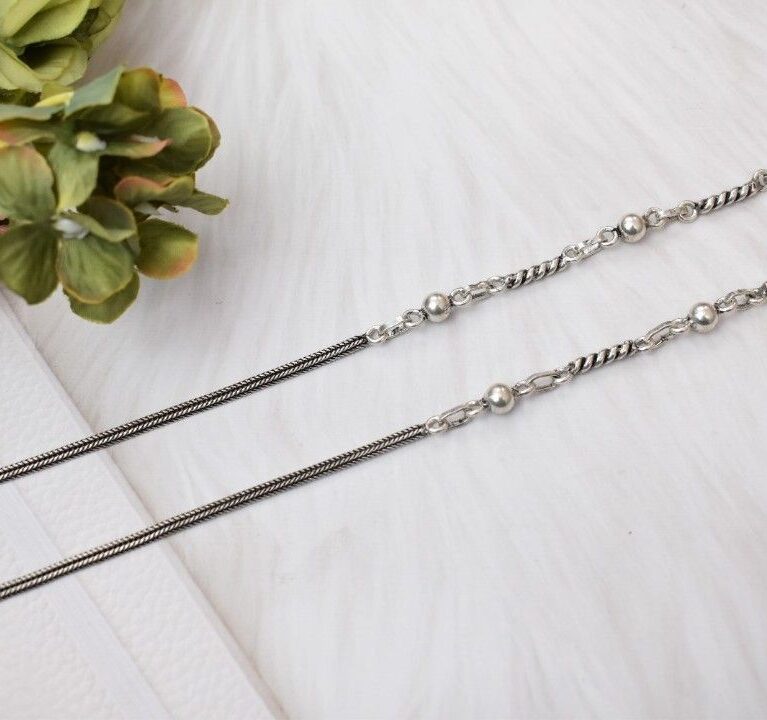 A pair of silver anklets with twisted chains and spherical beads.