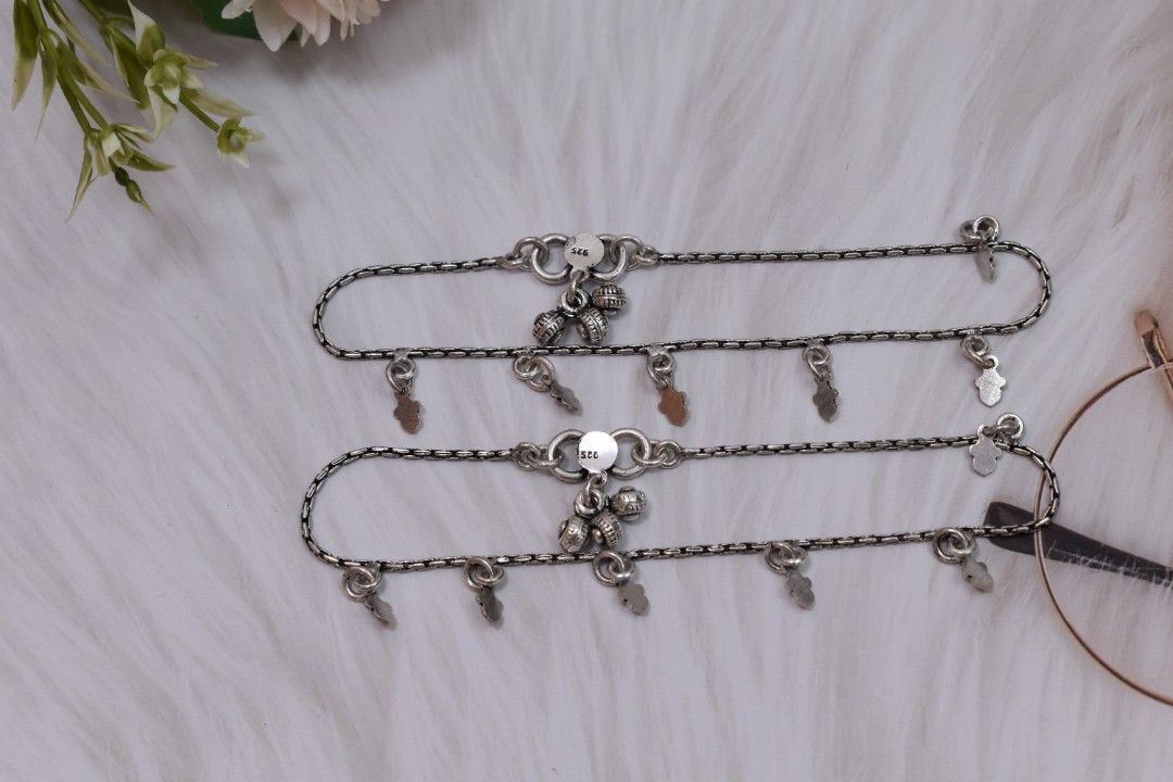 A pair of silver anklets with multiple hamsa hand pendants.