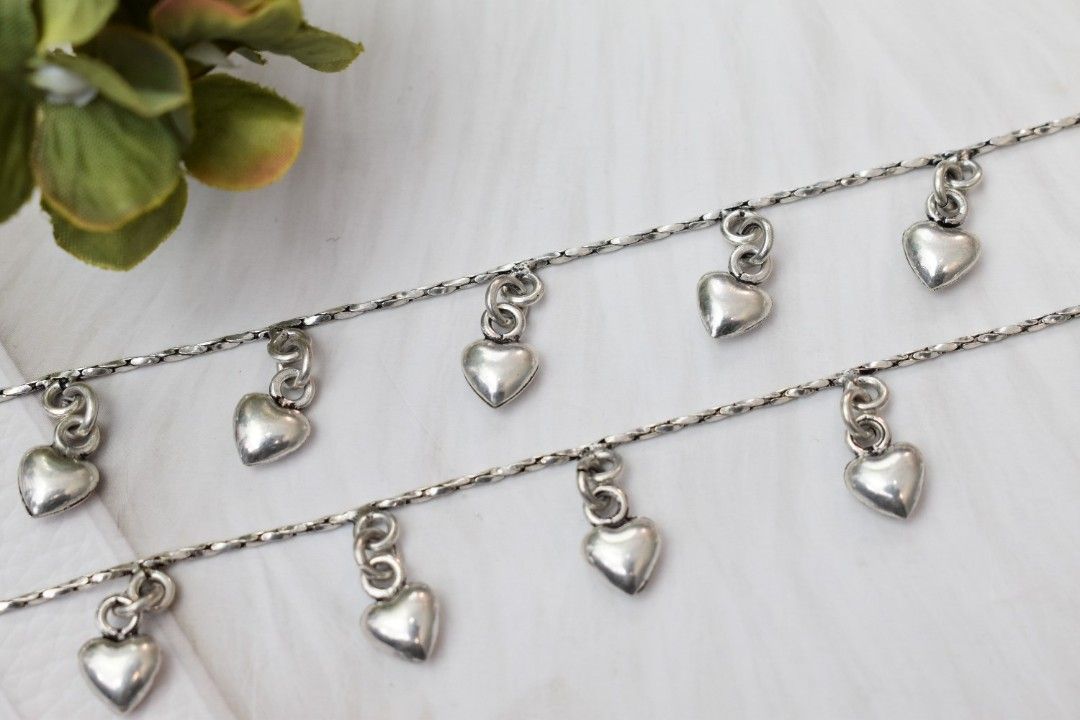 A pair of silver anklets with multiple heart-shaped pendants dangling from a delicate chain.