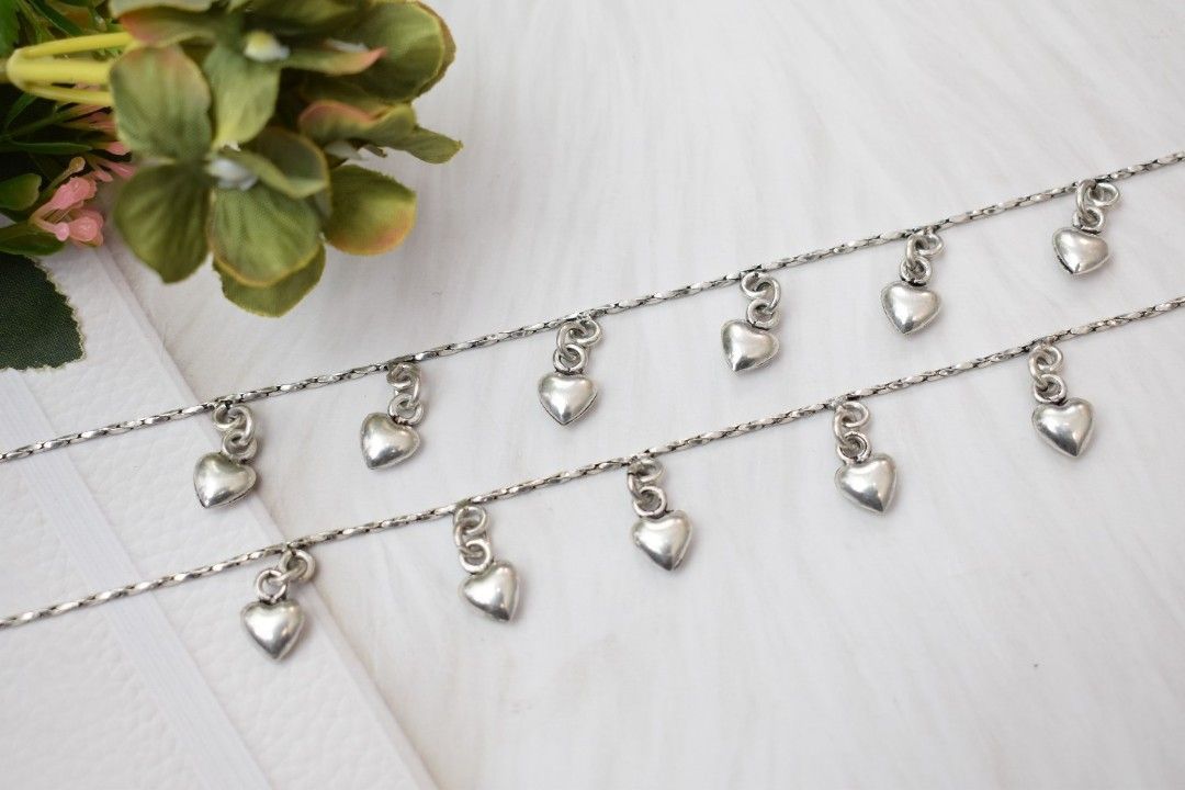 A pair of silver anklets with multiple heart-shaped pendants dangling from a delicate chain.