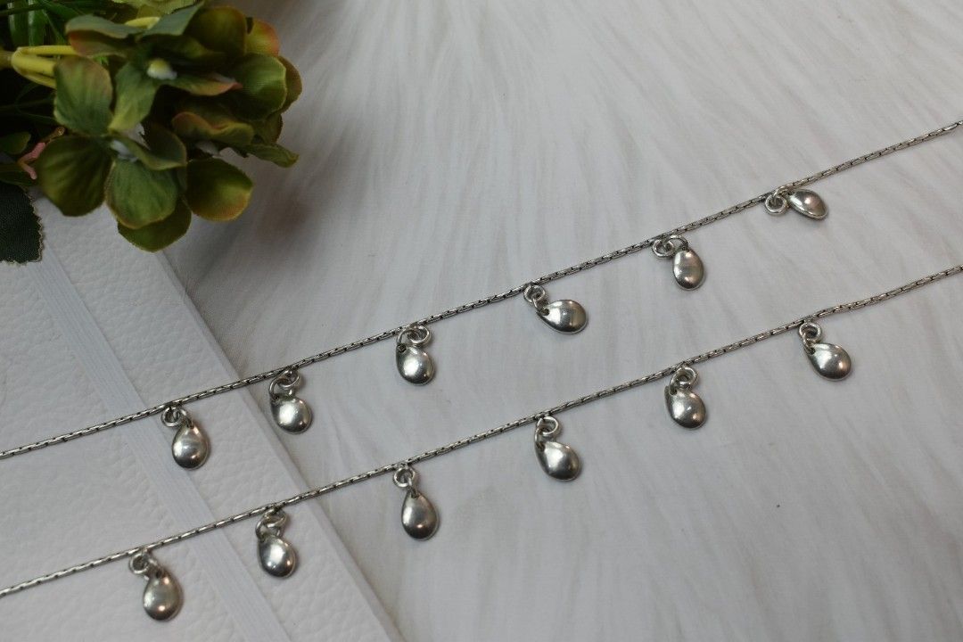 A pair of silver anklets with multiple teardrop-shaped pendants.