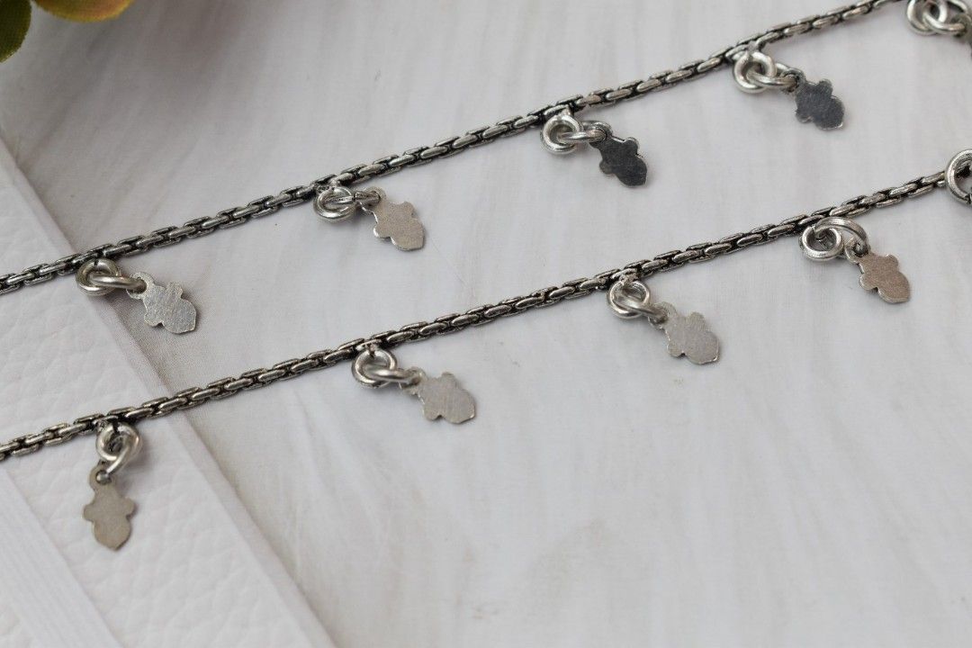 A pair of silver anklets with multiple hamsa hand pendants.