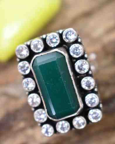 A silver ring with a rectangular green cutstone surrounded by white cutstones.