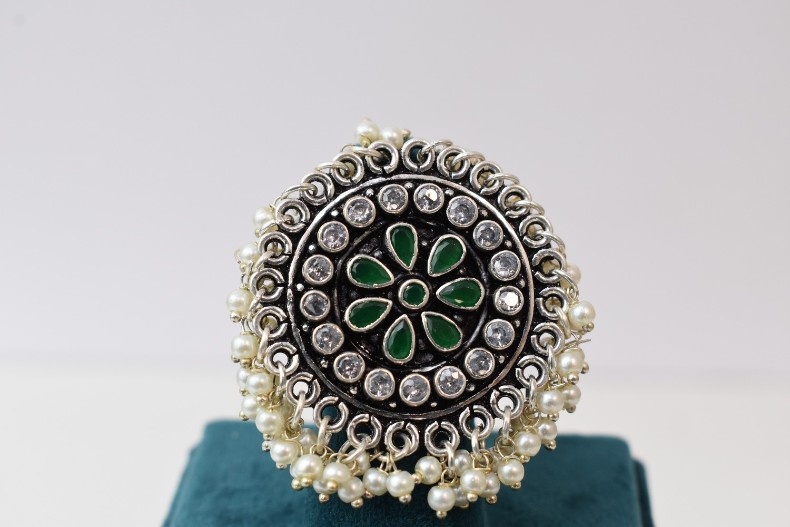 A silver ring with a circular design featuring green and white cutstones, adorned with pearls.