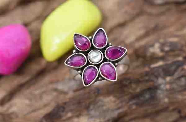 A silver ring with a flower-shaped design featuring pink cutstones and a white center cutstone.