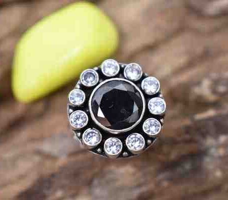 A silver ring with a circular design featuring a black cutstone surrounded by white cutstones.