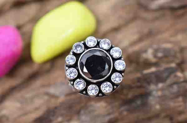 A silver ring with a circular design featuring a black cutstone surrounded by white cutstones.