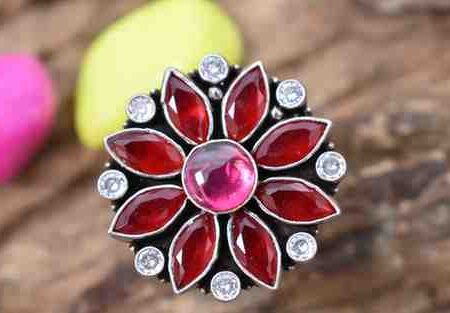 A silver ring with a floral design featuring red and pink cutstones surrounded by white cutstones.