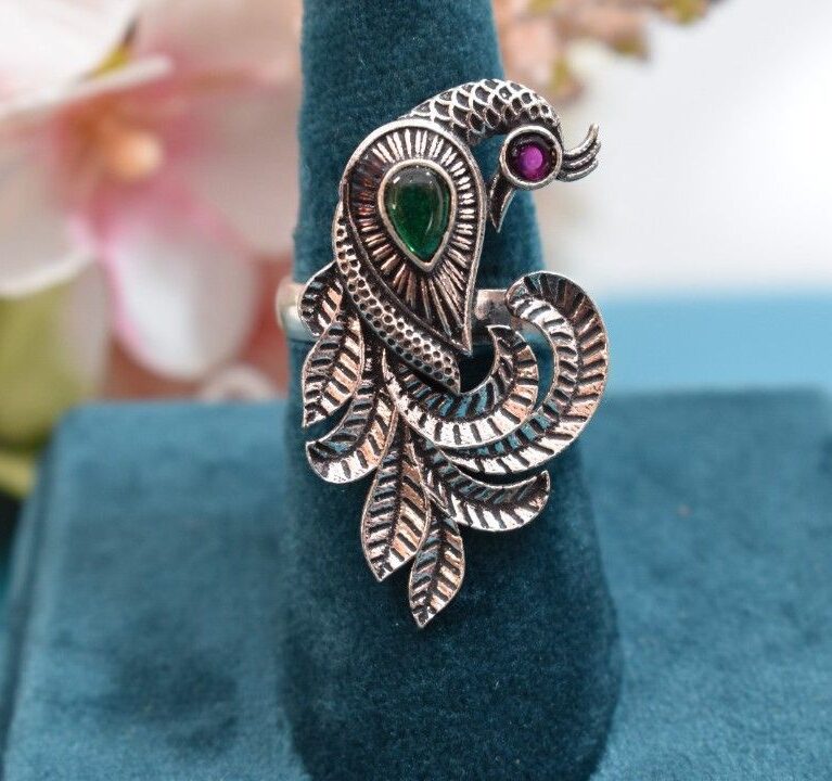 A silver ring featuring a peacock design with green and purple cutstones.