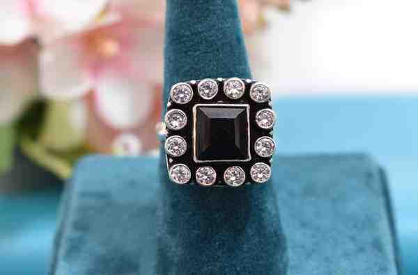 A silver ring with a square-shaped black cutstone surrounded by white cutstones.