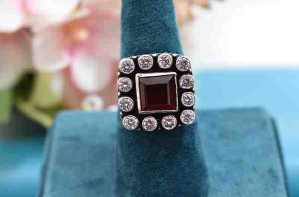 A silver ring with a square-shaped red cutstone surrounded by white cutstones.