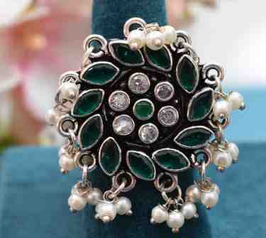 A silver ring with a circular design featuring green and white cutstones, adorned with pearls.