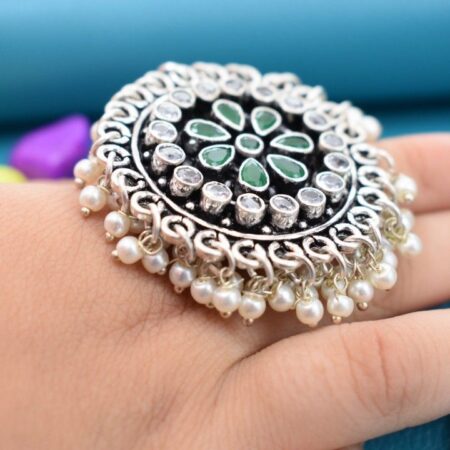 A silver ring with a circular design featuring green and white cutstones, adorned with pearls.