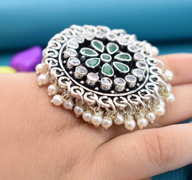 A silver ring with a circular design featuring green and white cutstones, adorned with pearls.